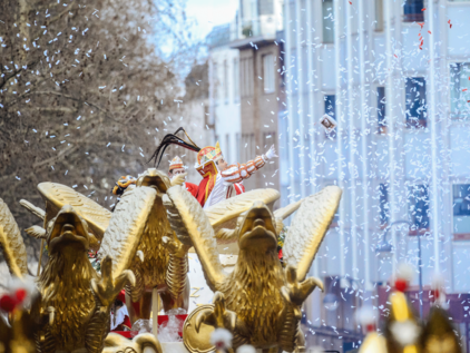 Prinz Karneval 2019 mit Konfetti im Rosenmontagszug Man sieht den Prinz Karneval auf seinem Festwagen im Rosenmontagszug 2019, er wirft eine Schachtel Pralinen. Rund um den Wagen ist weißes Konfetti zu sehen und im Vordergrund sind die goldenen Fabelwesen zu sehen, die den Wagen des Prinzen ziehen.