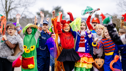 Bunt kostümierte Kinder springen in die Luft, heben die Hände zum Himmel und lachen.